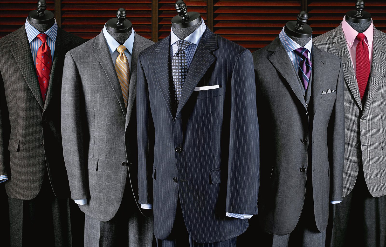 Five suits on dress forms against red shutters, each with a different shirt and tie.